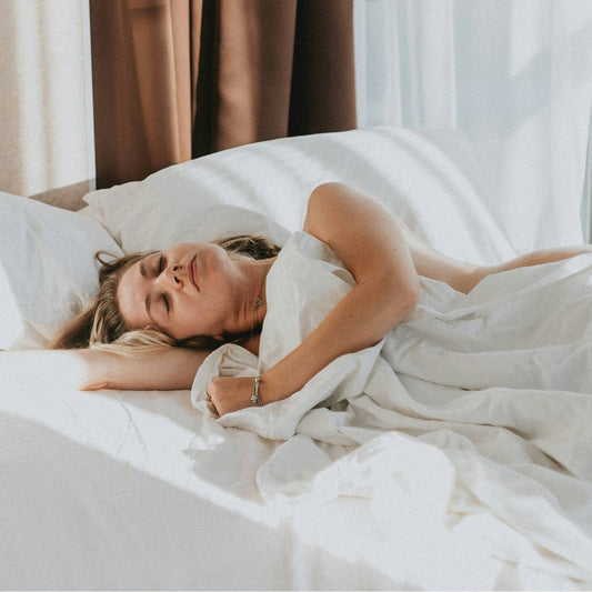 A woman sleeping on a bed with white linen and brown curtains in the background
