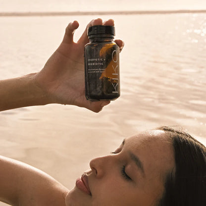 Person holding a bottle labeled Kiko Prebiotic & Probiotic near a body of water