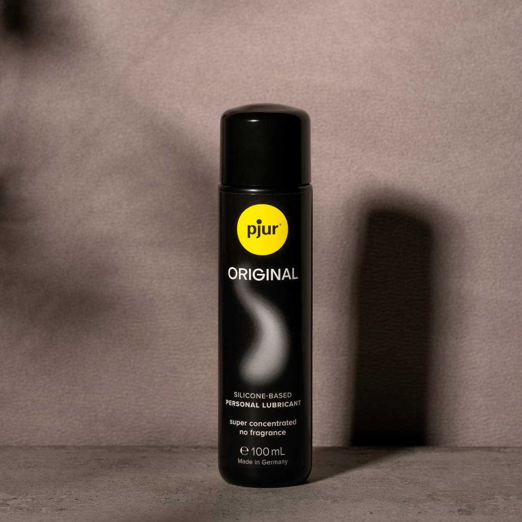 Black bottle of pjur Original lubricant with a yellow label on a gray background