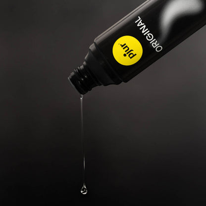 Black bottle with yellow label pouring a drop of liquid on a dark background