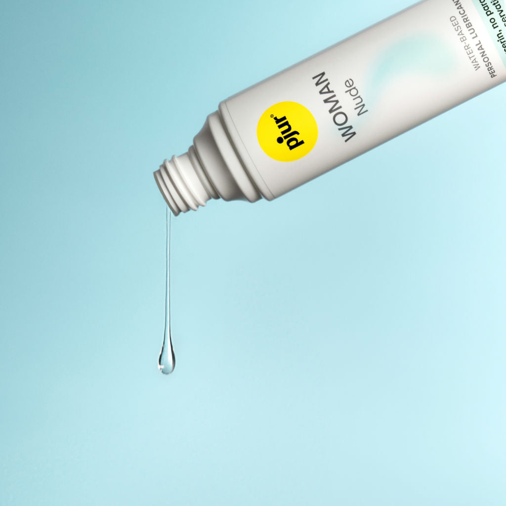 White bottle of pjur WOMAN Nude pouring the water-based lubricant on a light blue background