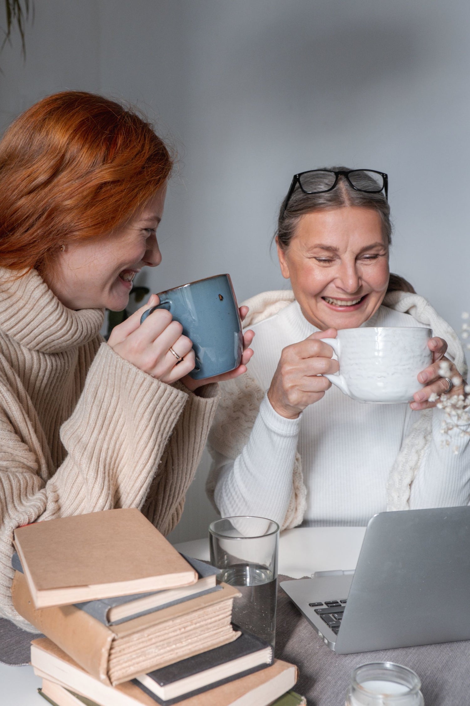 An image of two contented women in front of a laptop against a light grey  background, sharing an intimate moment together